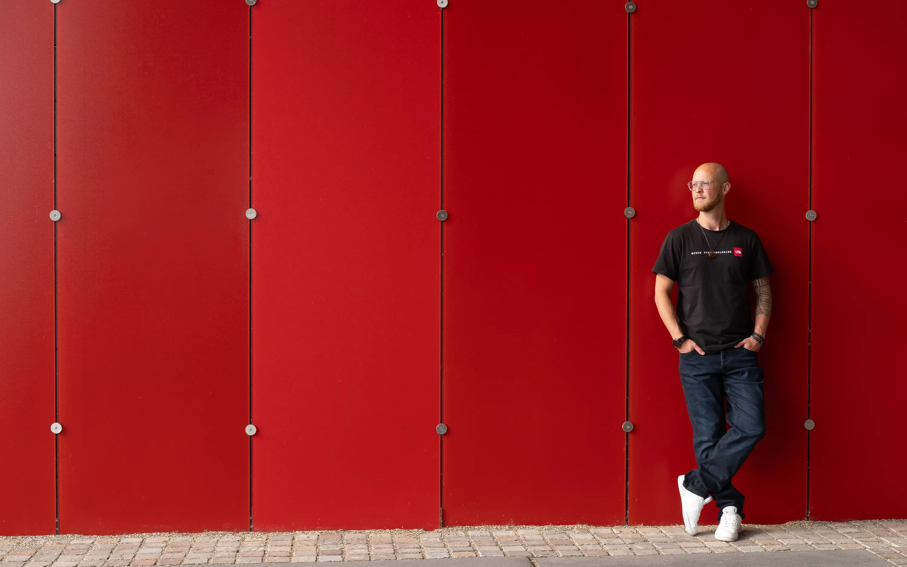 Merlijn Linschooten, fractional CMO for deep tech, leaning against a bright red wall at High Tech Campus Eindhoven
